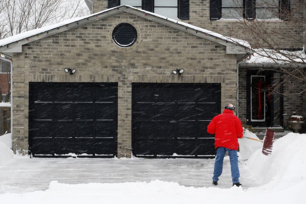 Image of a man shoveling snow out of his driveway in front of his garage